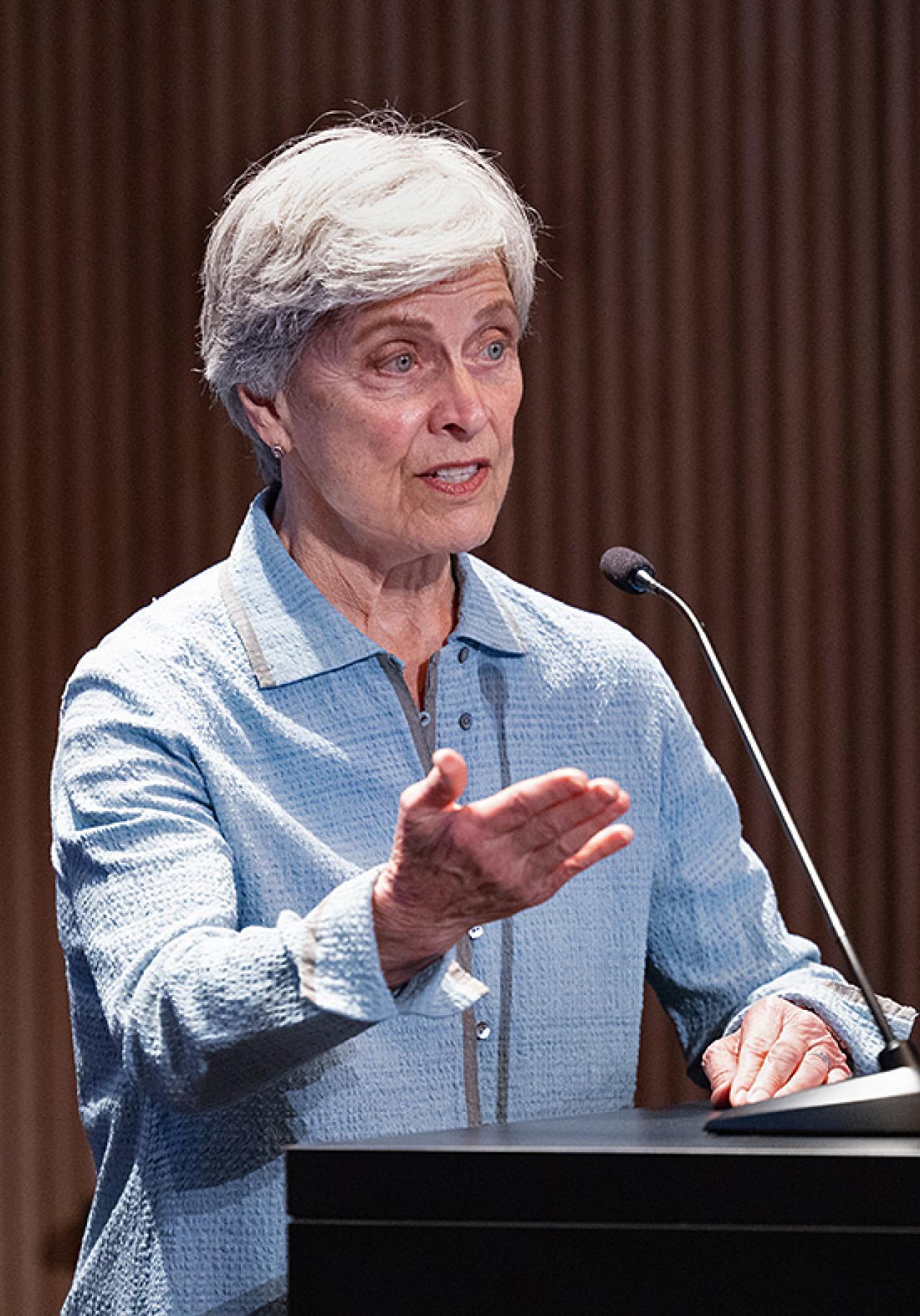 A woman with gray hair speaks at a podium