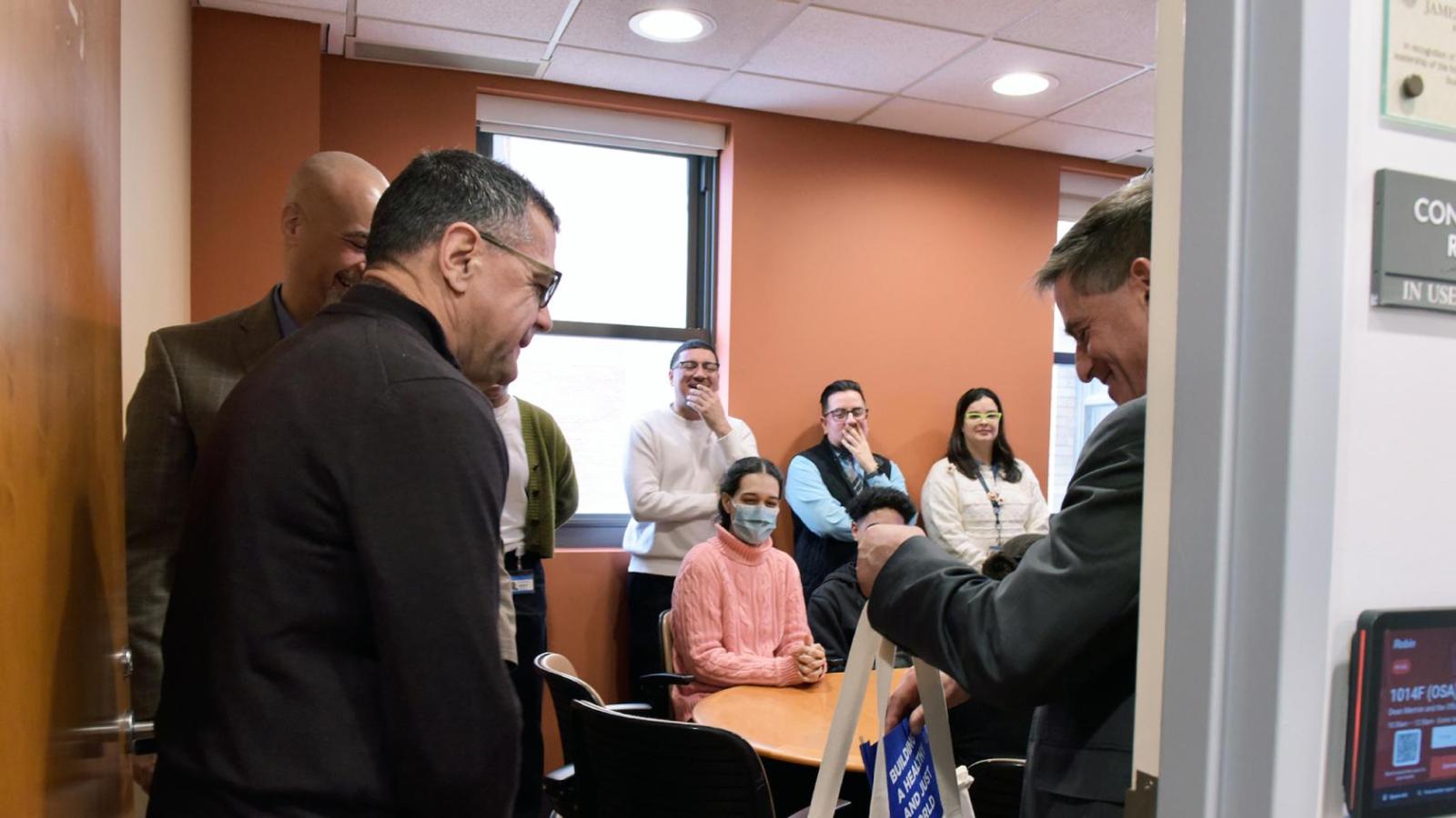 A smiling man looks at a canvas bag while others look on