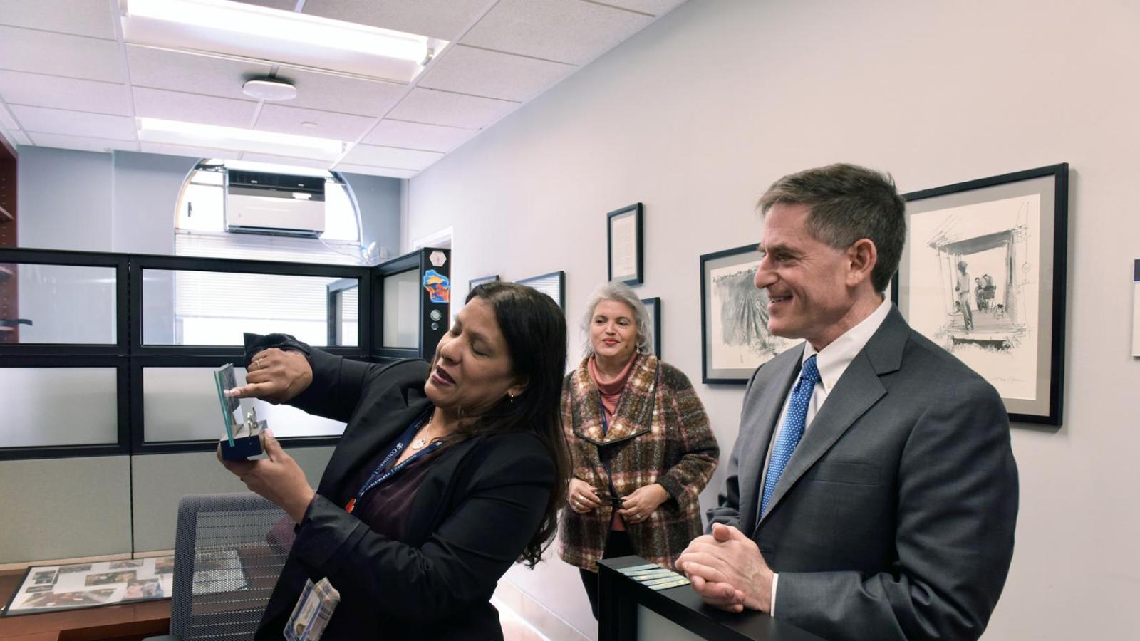 A woman points to a framed photo as a man in a suit and another woman look on
