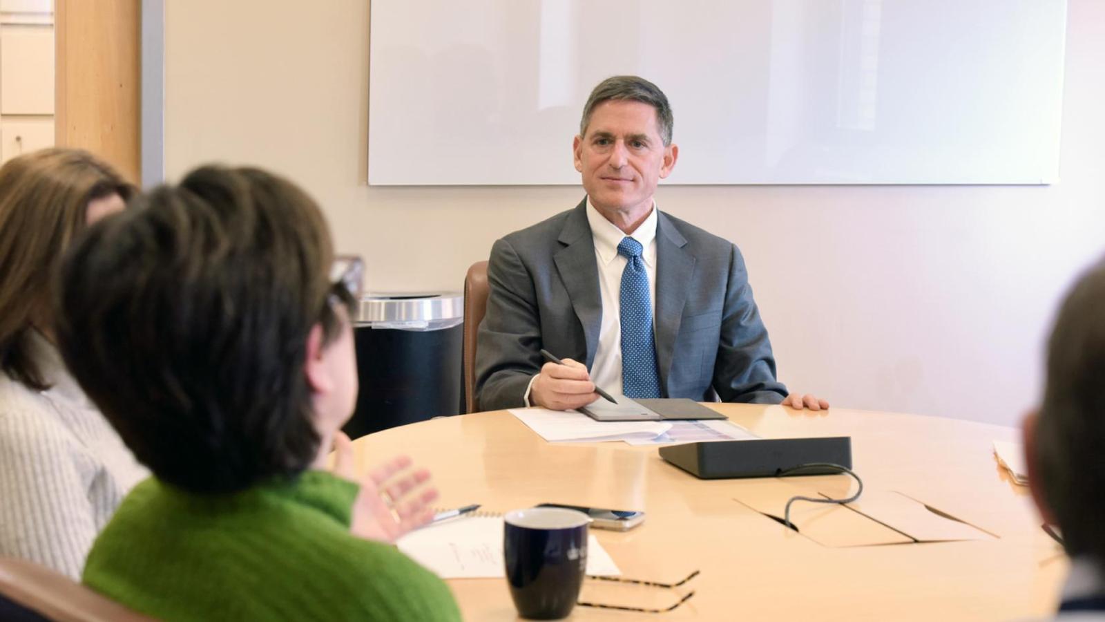 A man in a suit sits at the head of a conference table
