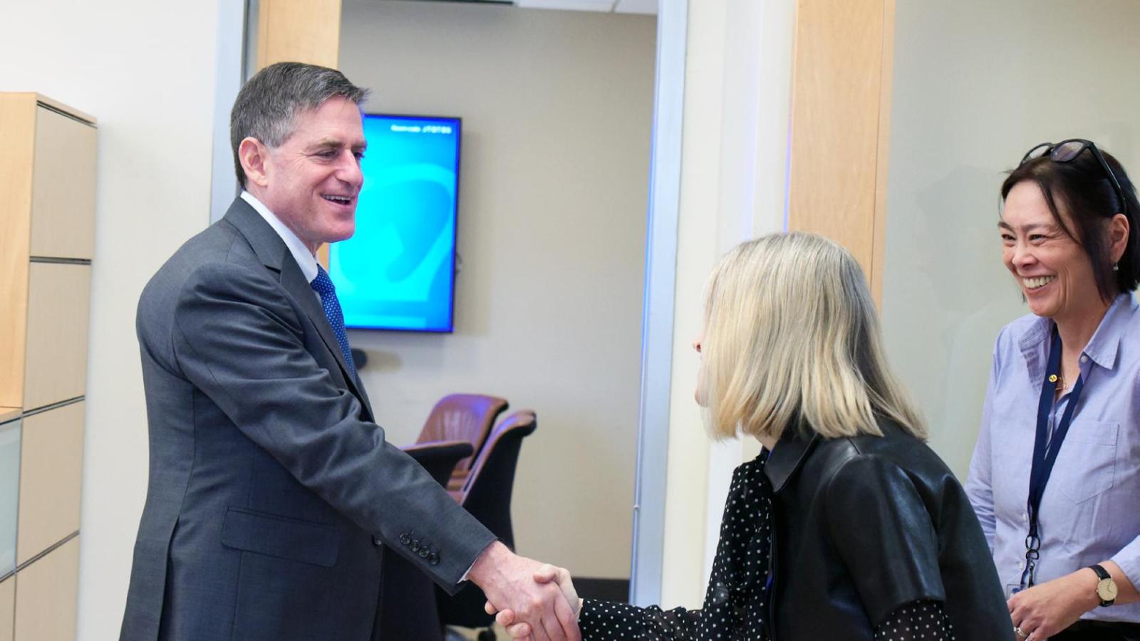 A man in a suit shakes hand with a woman as another smiling woman looks on
