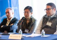 A seated woman speaks into a microphone with a man on either side