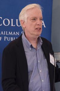 A man with white hair stands in front of a blue backdrop reading Columbia Mailman School of Public Health