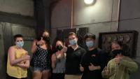 A group of students in casual clothes give a thumbs up outside an escape room