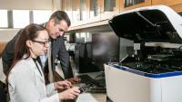 A student and faculty member review data on a computer next to lab equipment