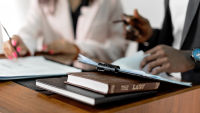 Two people are at a table. Only their torsos are visible. The photo focuses on a book on the table titled THE LAW.