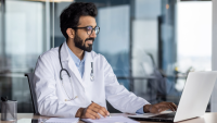 Male doctor smiling and using laptop