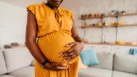 A photo of a pregnant Black woman in a yellow dress holding her belly