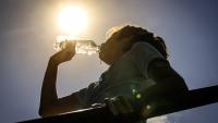 A girl drinks from a water bottle under a bright sun