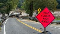 A flooded road with an orange sign reading, "Road Closed High Water."
