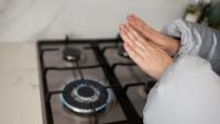 A woman wearing a coat warms her hands over a gas stove