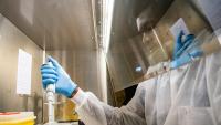 A Black man wearing PPE using a pipette in a laboratory