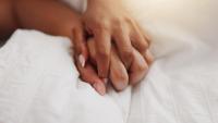 A couple's interlaced hands on a bed