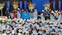 A wide-angle image of graduates in blue cap and gown receiving diplomas