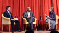 A photo of two men and one woman seated on a stage in conversation
