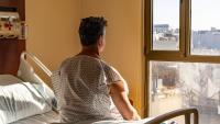 Man in hospital bed looking out at city; worrying about homelessness