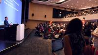 A man at a podium addresses an auditorium full of people