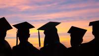 A silhouette of five people wearing mortarboard hats against a pink and orange sky
