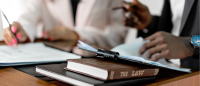 Two people are at a table. Only their torsos are visible. The photo focuses on a book on the table titled THE LAW.