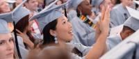 A young woman applauds in a group of graduates wearing blue cap and gown