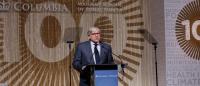 Lee Bollinger speaks at a podium in front of a Columbia Mailman Centennial 100 logo