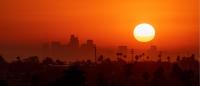 An orange sky and a setting sun with a background of buildings and palm trees