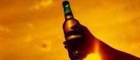 A backlit hand and arm holding a beer bottle to the sky