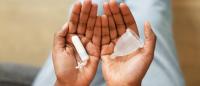 Black hands palms up hold a tampon and a menstrual cup