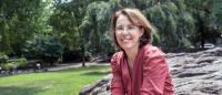 Smiling woman in red blouse (Navas-Acien) sits on a rock in a park