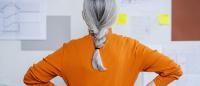 Woman with grey ponytail looks a bulletin board