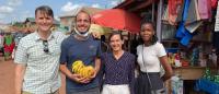 Four people pose for a photo in a marketplace setting (one man holds bananas))