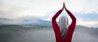 A woman with grey hair in a red shirt presses her hands together over her head