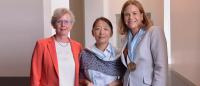 Three women pose for a photo, one holding an engraved crystal object and the other wearing a medal
