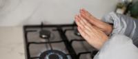 A woman wearing a coat warms her hands over a gas stove