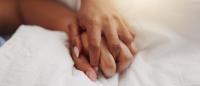 A couple's interlaced hands on a bed