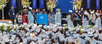 A wide-angle image of graduates in blue cap and gown receiving diplomas
