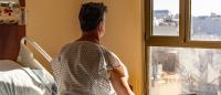 Man in hospital bed looking out at city; worrying about homelessness