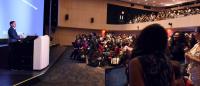 A man at a podium addresses an auditorium full of people
