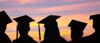 A silhouette of five people wearing mortarboard hats against a pink and orange sky