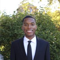 Man in suit and tie standing in front of a hedge