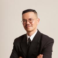 Portrait of a person in glasses seated indoors in a dark suit.